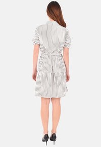 Vestito a righe corto con maniche a palloncino corte, vita cintata, gonna a strati e orlo sopra il ginocchio. Schema di colori in bianco e nero.