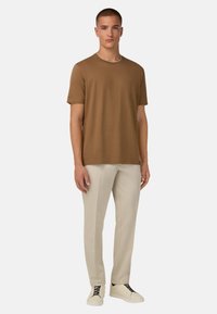 Ruda trumpa rankovė t-shirt su apvalia iškirpte, derinama su smėlio spalvos kelnių ir baltais sportbačiais. Paprastas dizainas, minkšta tekstūra ir laisvas pritaikymas.