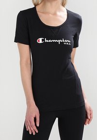 Svart kortärmad t-shirt i bomullsmix med rund halsringning och "Champion U.S.A."-logotyp i vitt och rött på framsidan.