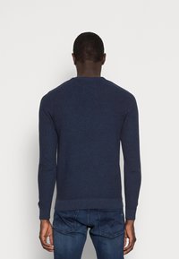 Marinblå stickad tröja med långa ärmar och rund halsringning. Har en texturerad tyg och ribbad fåll. Bärs med blå jeans.