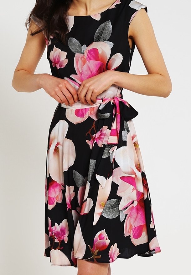 Ärmlös svart klänning med stora rosa och vita blommönster, figursydd midja knuten med ett matchande bälte i tyg.