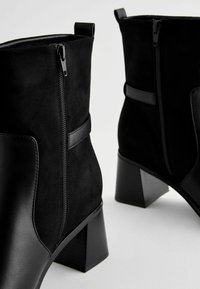 Bottines noires en cuir lisse et en daim, dotées d'une fermeture éclair sur le côté, de talons carrés et d'un design minimaliste.