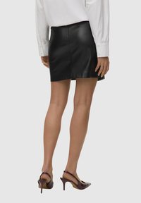 Jupe en cuir noir mini, avec une coupe droite et des coutures minimales, associée à des chaussures à talons hauts violettes et une chemise blanche à boutons.