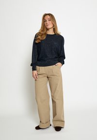 Maglione lavorato a maglia color blu navy con un leggero luccichio, scollo arrotondato e maniche ampie, abbinato a pantaloni beige a vita alta e gamba larga.