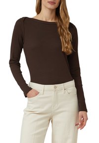 Brązowa bluzka z długim rękawem i dekoltem typu łódka, wykonana z miękkiego, elastycznego materiału, zestawiona z jasnymi, wysokim stanem jeansami.