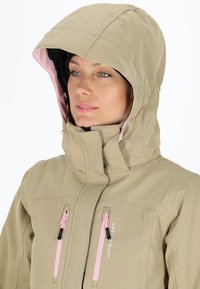 Giacca beige con cappuccio, caratterizzata da dettagli rosa. Ha due tasche con zip e un colletto alto, realizzata in un tessuto dalla superficie liscia.