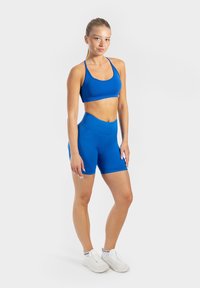 Blauwe sportoutfit met een aansluitend tanktop en hooggeplooide shorts, gemaakt van rekbaar materiaal. Witte sportschoenen.