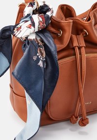 Sac en cuir marron avec cordon de serrage, foulard en soie bleu et blanc à motifs attaché à une anse et poche avant zippée.
