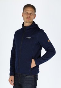 Felpa con cappuccio navy con finitura testurizzata, zip intera, tasche frontali e logo sul petto. Presenta un design aderente e cappuccio.