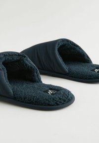 Chaussons bleu marine avec une doublure en polaire douce et texturée, un design ouvert sur le devant et des semelles en caoutchouc flexibles. Présence d'un logo sur le pied.
