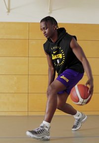 Melna bez piedurknēm kapuce ar "Lakers" logotipu, purpura sporta šorti, pelēkas sporta kurpes, driblējot basketbola bumbu uz koka sporta zāles grīdas.