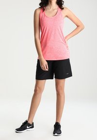 Pink, sleeveless athletic tank top with a textured look paired with black athletic shorts. Model wearing black sneakers.