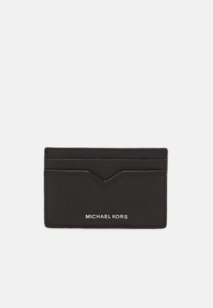 Black leather cardholder with textured surface, featuring five slots and a chevron accent. "MICHAEL KORS" embossed at the bottom.