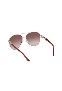 Ochelari de soare tip aviator cu lentile gradient maro, cadru din metal argintiu și brațe din plastic burgundy, cu numele mărcii "GUESS" scris în alb.