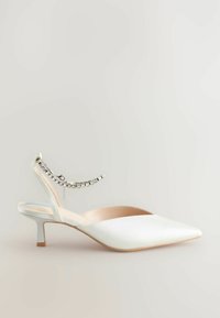 Valkoinen satiininen slingback-kenkä, jossa on terävä kärki, takana koristeellinen nilkkahihna, jossa on strassikoristeita, sekä matala stiletto-kanta.