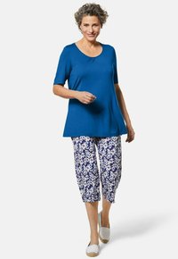 Blaues kurzärmeliges Oberteil mit Rundhalsausschnitt, kombiniert mit blauen und weißen floral bedruckten Caprihosen, ergänzt durch helle Slipper.