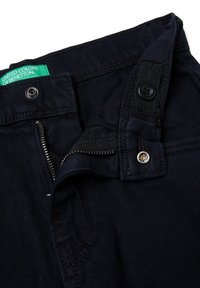 Tmavě modré džínové kalhoty s částečně otevřeným zipem, knoflíkem, zapínáním na patentky a viditelnou zelenou cedulkou "United Colors of Benetton".