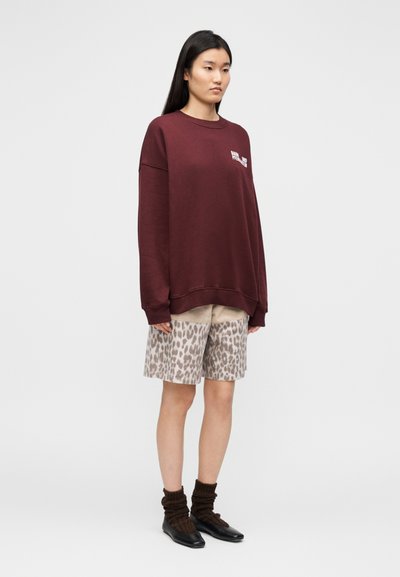 Μπορντό φαρδιά φούτερ, μπεζ σορτς με λεοπάρ μοτίβο, καφέ ριγωτές κάλτσες και μαύρα παπούτσια. Απλός σχεδιασμός με χαλαρή εφαρμογή και αντιθετικά σχέδια.