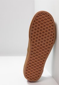 Semelle de chaussure en caoutchouc marron avec un motif de grip en forme de diamants, présentant un bord lisse et arrondi ainsi qu'une légère pente vers le haut sur un côté.