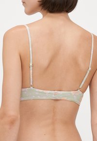 Grønn bikini-overdel med blomstermønster, tynn justerbare stropper og detaljer i gullmetall. Glatt tekstur med en tettsittende design.