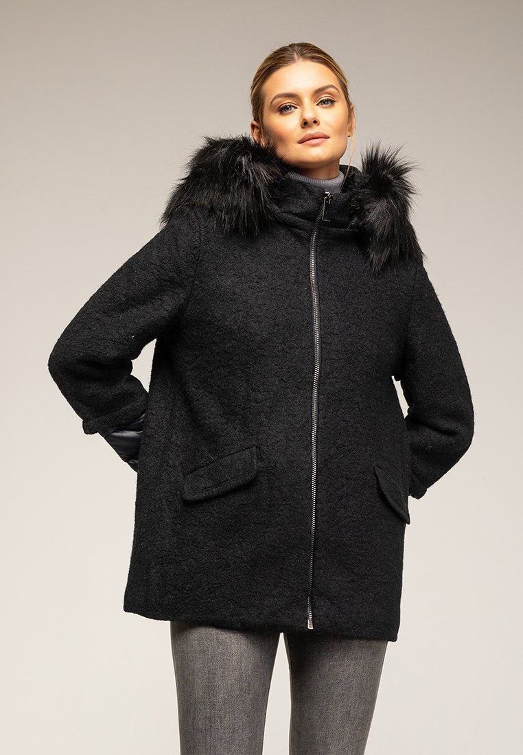 Czarny płaszcz z mieszanki wełny z kapturem z sztucznego futra, zapinany na zamek, z dwiema przednimi kieszeniami i luźniejszym krojem. Tekstura wydaje się miękka i strukturalna.