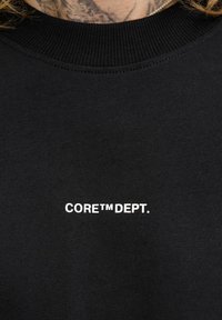Sort sweatshirt med ribbet halsudskæring og hvid tekst, der står "CORE™ DEPT." på forsiden. Stoffet ser glat ud med en ensartet tekstur.