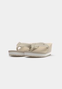 Beige kilehæle sandaler med en glat tekstureret fodseng, tynde remme og en kontrasterende hvid mellemsål. Har et mærke logo på remmen.