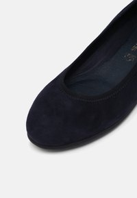 Gros plan d'une ballerine en suédine bleu marine avec un bout arrondi et une bordure noire autour de l'ouverture.