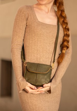 Kleine olivgrüne Leder-Crossbody-Tasche mit Reißverschluss und goldenen Akzenten, die eine runde Form und subtile Nähdetails aufweist.