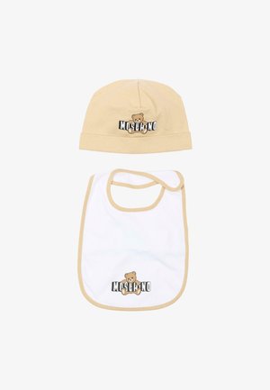 Chapeau de bébé beige et bavoir blanc avec bordure beige, tous deux ornés d'un logo d'ours en peluche et du texte "MOSCHINO" sur un fond blanc.