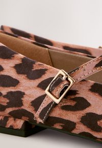 Chaussures plates à imprimé léopard avec une surface en tissu doux, des nuances de marron et beige, et un détail boucle de couleur dorée sur la bride.
