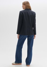Blazer bleu marine foncé en tissu texturé, à simple boutonnage, avec revers crantés, associé à un jean en denim bleu taille haute et des baskets décontractées.