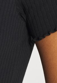 Haut noir à manches courtes et côtelé avec un ourlet ondulé. La texture est douce avec des lignes verticales subtiles, mettant en valeur un design ajusté.