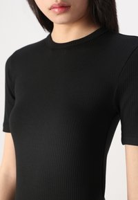 Top corto a maniche corte nero a coste con scollatura tonda, caratterizzato da un design aderente che mette in evidenza la texture e la forma.
