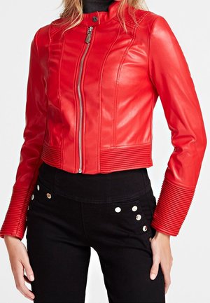 Mujer con chaqueta de cuero roja ajustada con cremallera frontal y detalles acanalados en los puños y la cintura, combinada con pantalones negros con tachuelas plateadas.