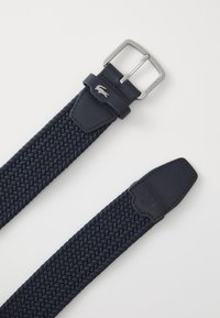 Navy woven belt with leather accents, silver metal buckle, and logo detail on the leather end. Textured fabric body for flexibility.