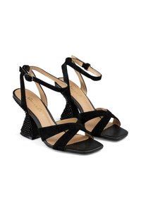 Sandalias de tacón alto de ante negro con cintas transversales anchas, correa al tobillo, puntera cuadrada y tacón en forma de cono texturizado con detalles de tachuelas.