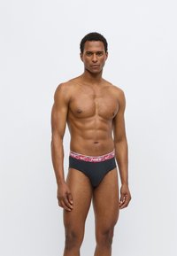 Černé slipy s červenobílým logem Nike na pásku. Látka vypadá hladká a elastická, navržená pro těsné přilnutí.