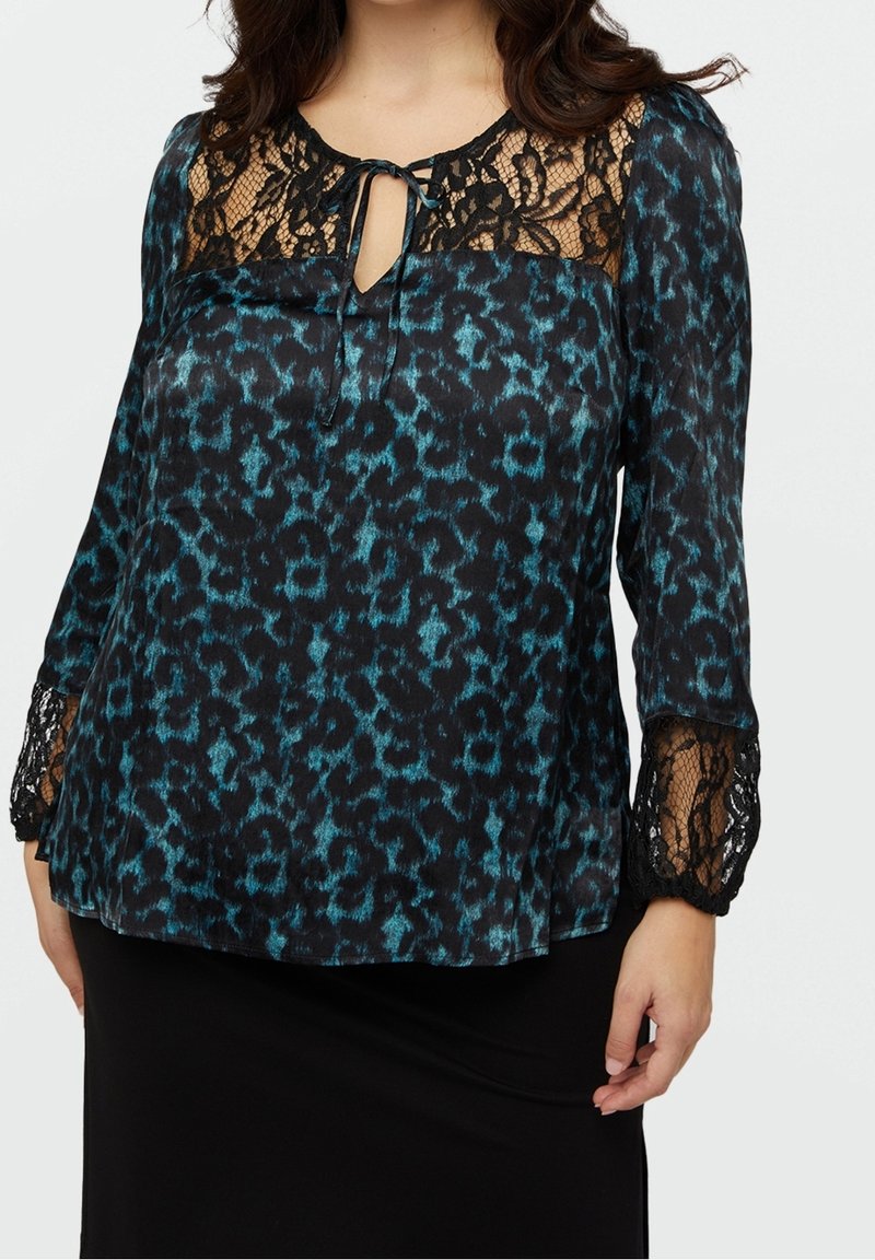 Blouse noire à imprimé léopard bleu, avec empiècement en dentelle et manches, col à nouer, et tissu texturé. Coupe ample avec manches longues.