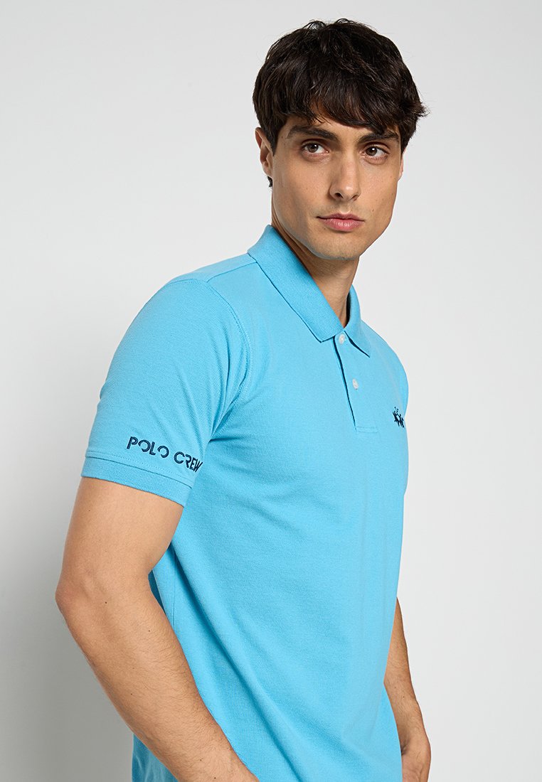 Lichtblauw poloshirt met korte mouwen van katoen, met een kraag, een merkopdruk op de mouw en een aansluitende pasvorm.