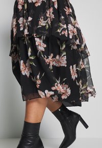 Gonna floreale nera a strati con fiori rosa e verdi, abbinata a stivali neri in pelle al ginocchio con zip laterale e tacco largo.