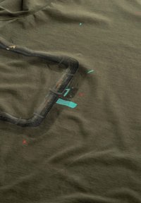 T-shirt olive en coton doux, avec un design graphique représentant un tuyau noir, agrémenté d'accents rouges et turquoise.