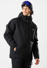 Schwarze isolierte Jacke aus Softshell-Material, mit Kapuze, Reißverschluss-Taschen und einem Logo auf der Brust. Glatte Textur.