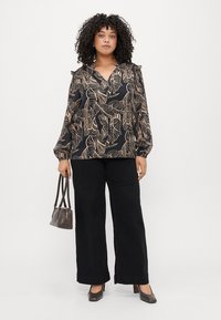 Blusa preta com padrão de folhas bege, decote em V e mangas longas bufantes. Combinada com calças largas pretas e uma pequena bolsa castanha.