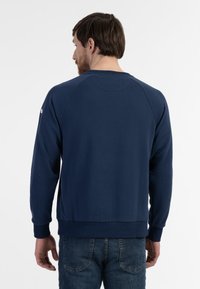 Mørkeblå sweatshirt lavet af blødt stof, med rund hals, raglanærmer og ribbede mansjetter og kant. Bagfra fremhæves den glatte tekstur.