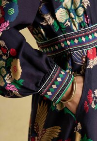 Tumedal lilledega kleit sisaldab erksate tikanditega, elastsete mansettide ja mustriga äärtega ning nähtavat taskut vöökoht. 