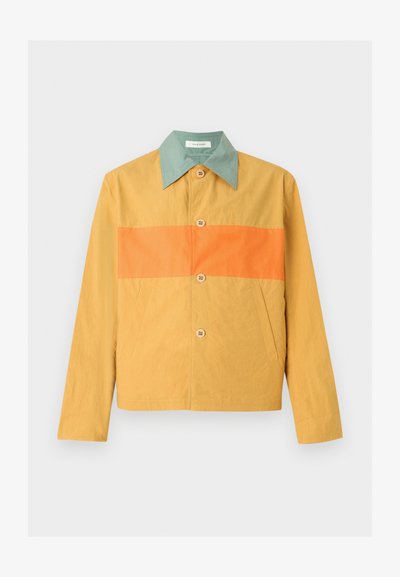 Κίτρινο τζάκετ με φαρδιά πράσινη γιακά, οριζόντια πορτοκαλί ρίγα στο στήθος, κλείσιμο με κουμπιά μπροστά και πλαϊνές τσέπες σε λευκό φόντο.