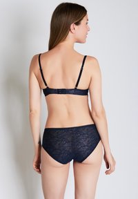 Navy lace bra and brief set with floral pattern, adjustable straps, and scalloped edges. Soft, textured fabric complements the design.