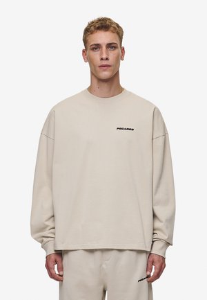 Beige sweatshirt met verlaagde schouders, ribgebreide manchetten en een minimalistisch ontwerp. Zwart "PEGADOR" logo op de borst. Zachte, katoenen structuur.