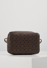 Borsa sintetica marrone con texture e motivo logo ripetuto, forma rettangolare, chiusura con zip e manici di un beige chiaro. Presenta due anelli laterali.